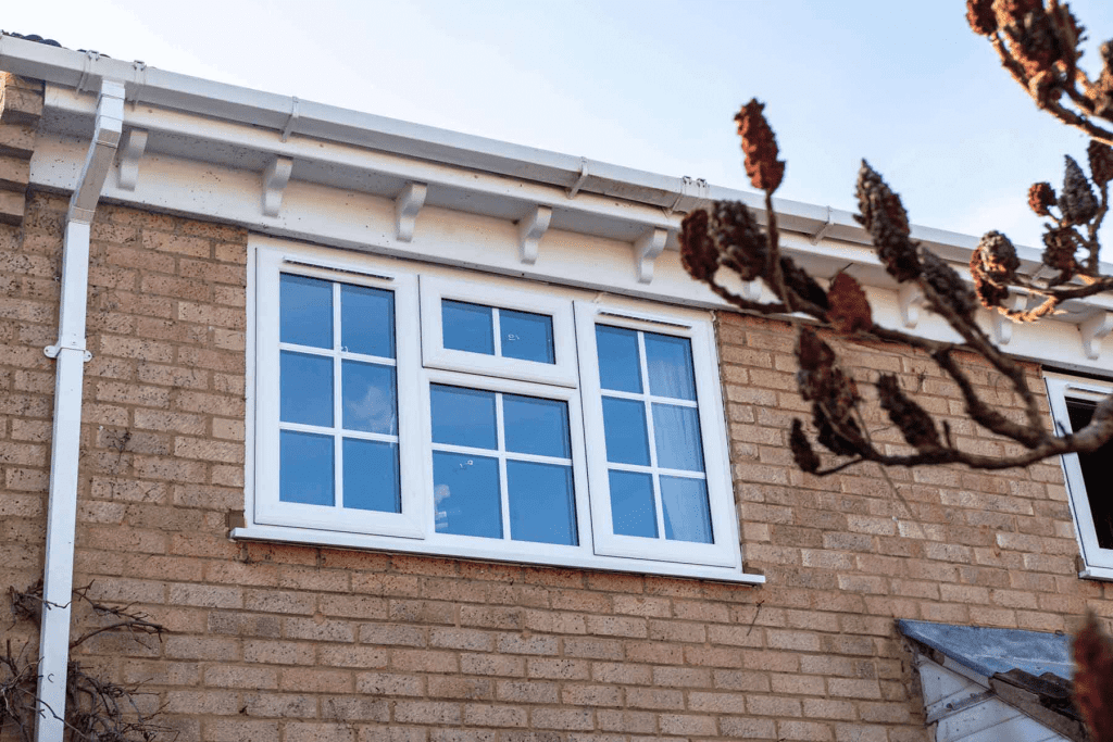 A white Georgian window uPVC triple-paned window installed in a brick house exterior, with part of a bare tree branch visible in the foreground.