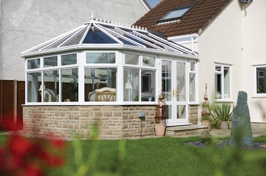 White Victorian conservatory with a stone base attached to a house in Aspley Heath, overlooking a garden