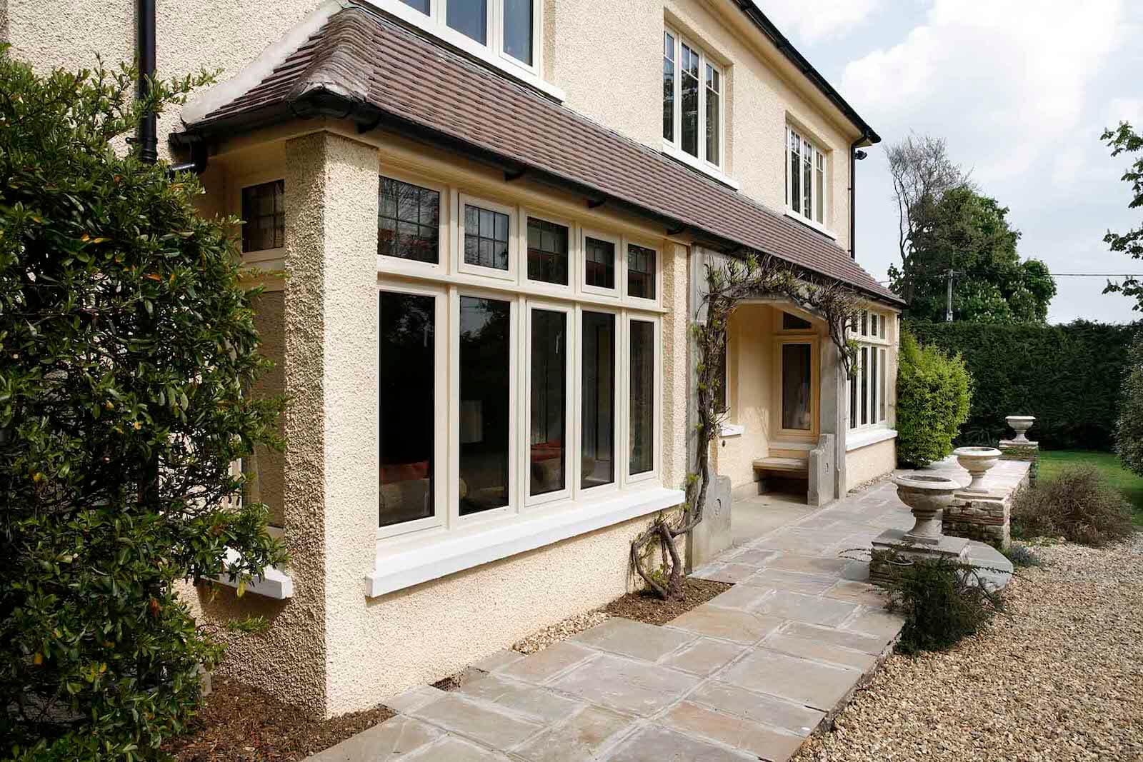 Cream flush casement double glazed windows on a traditional British home with a paved walkway.